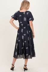 woman wearing a navy blue embroidered midi dress with short puff sleeves and a tiered skirt