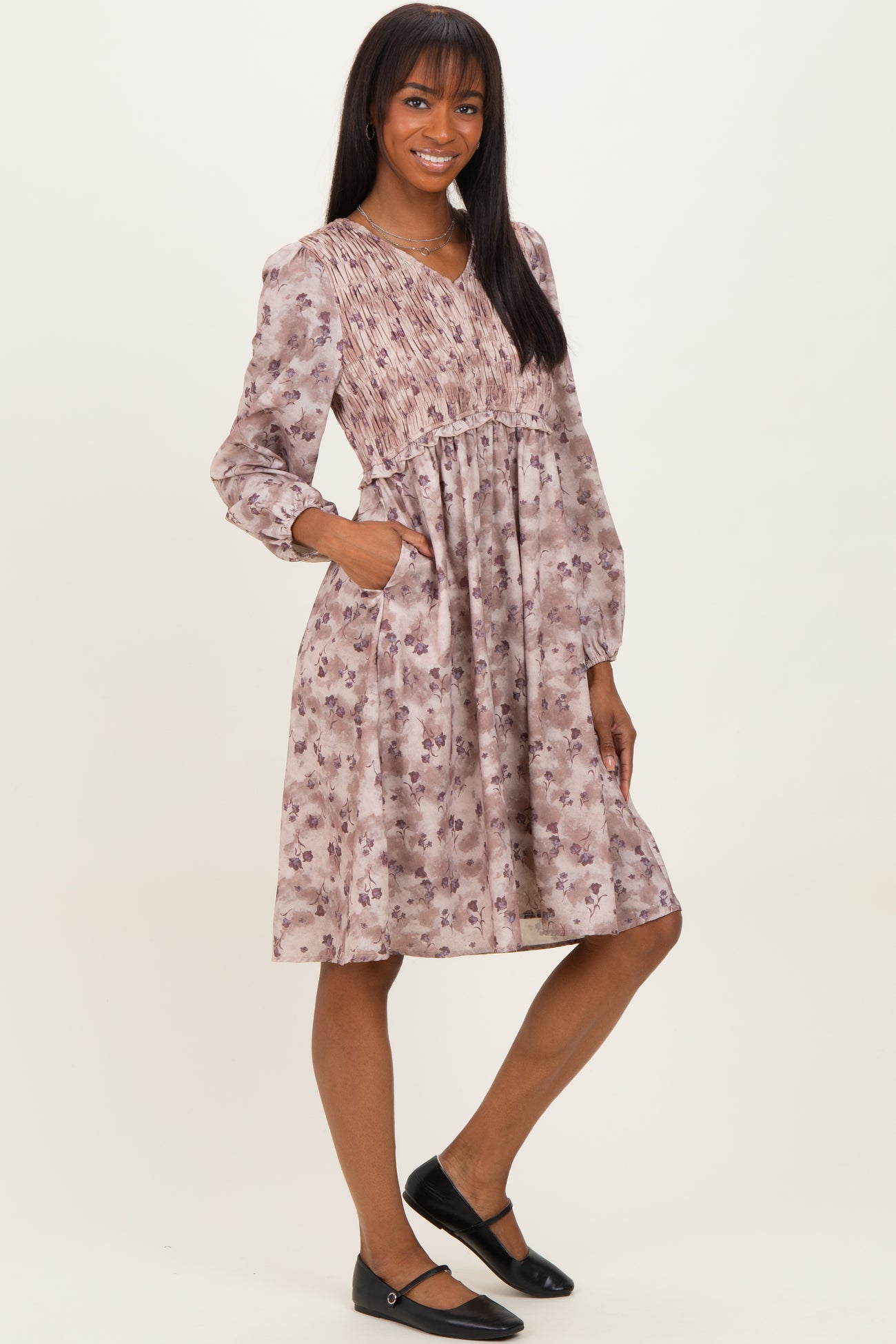 woman wearing a floral smocked midi dress in shades of pink with long sleeves and pockets