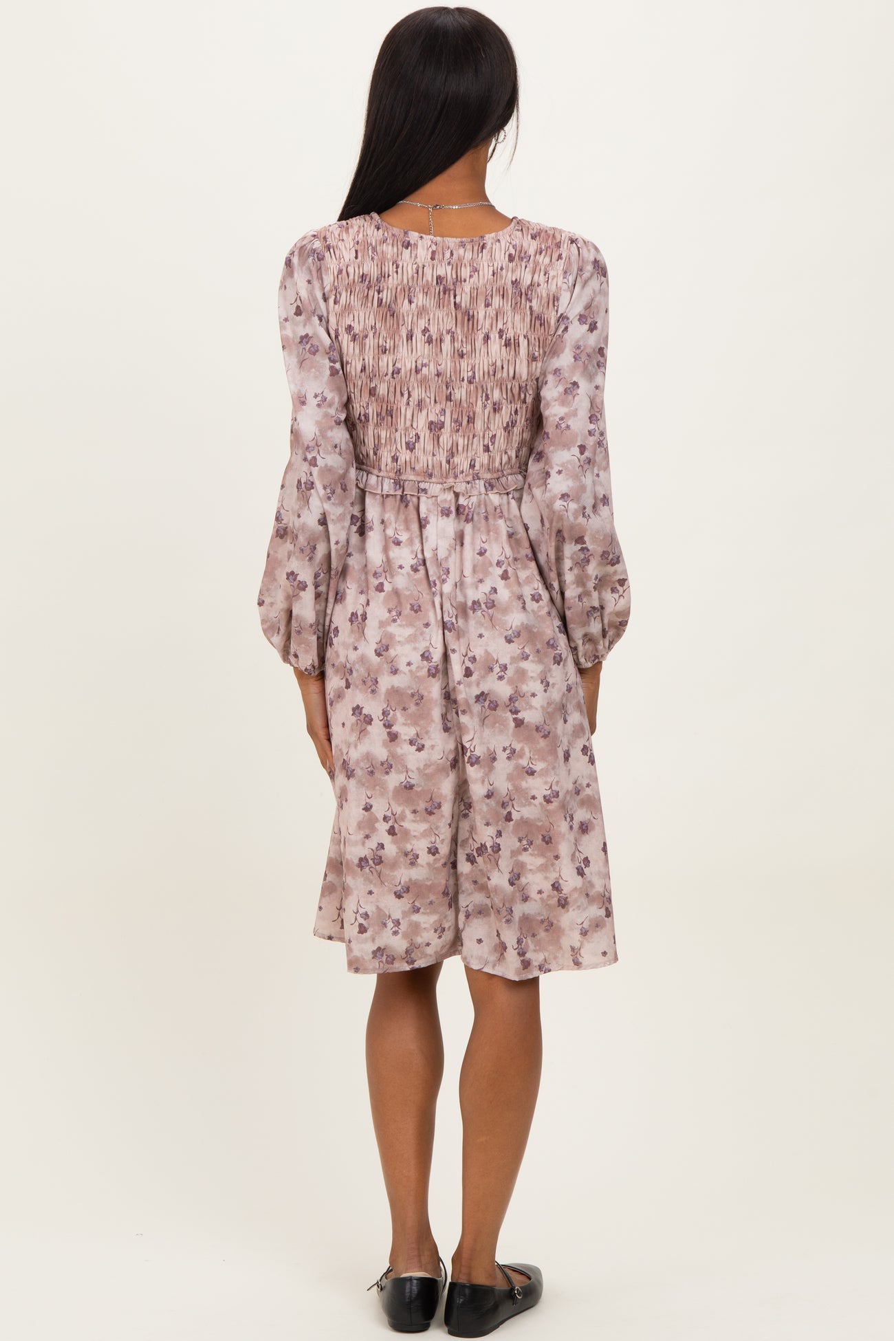 woman wearing a floral long sleeve dress with a smocked back and flared sleeves, viewed from the back