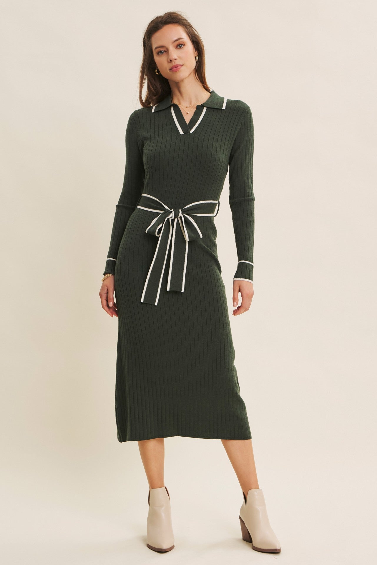 woman wearing a dark green ribbed midi dress with a collar and contrast tie at the waist, styled with ankle boots