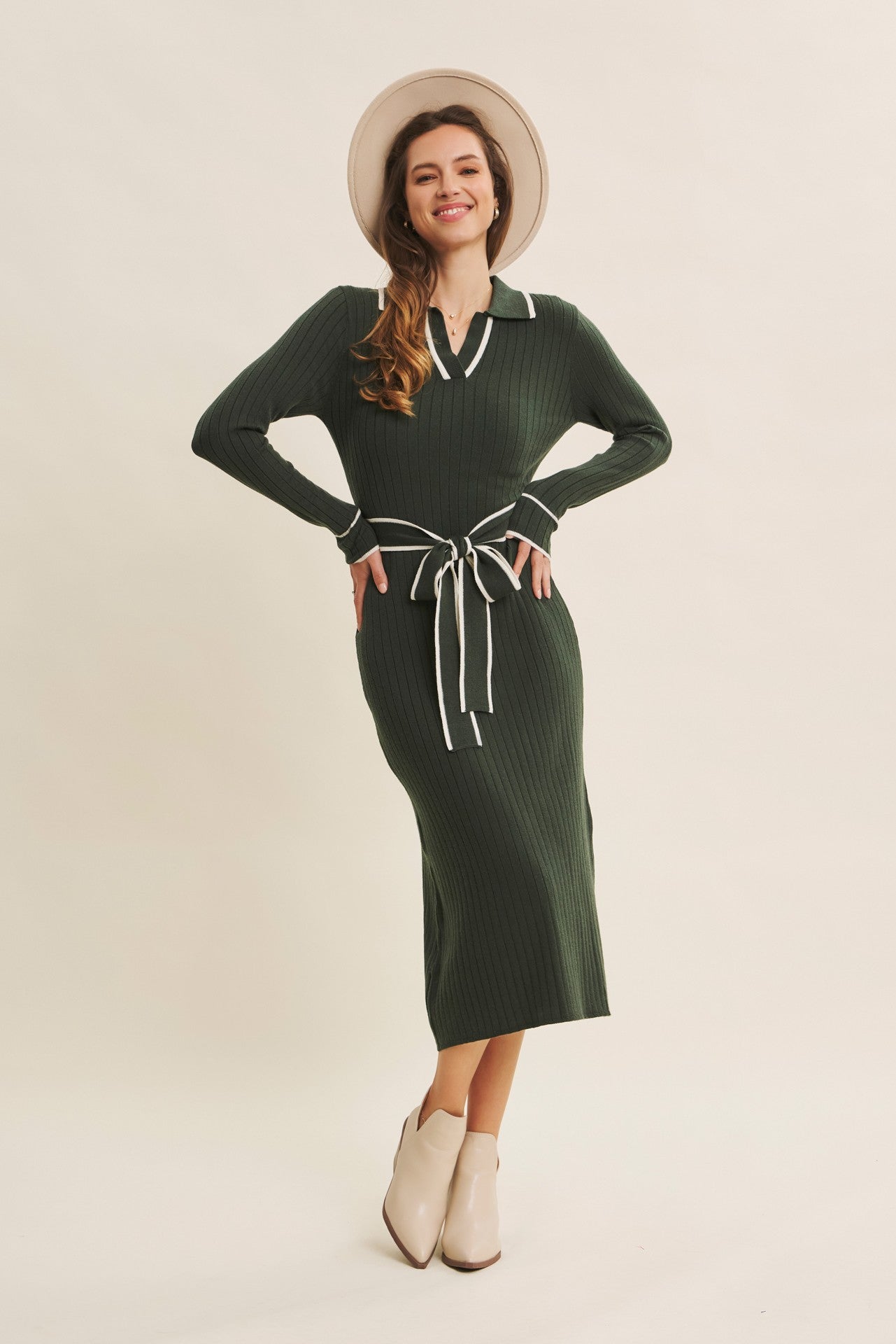 woman wearing a green ribbed midi dress with white collar and tie waist, paired with a hat and ankle boots