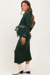 woman wearing a dark green ribbed maternity dress with a tie waist, showcasing her baby bump