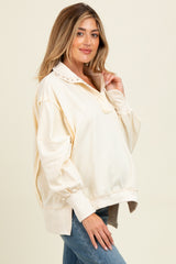 woman wearing a cream maternity pullover with a collar and button details, showcasing her baby bump