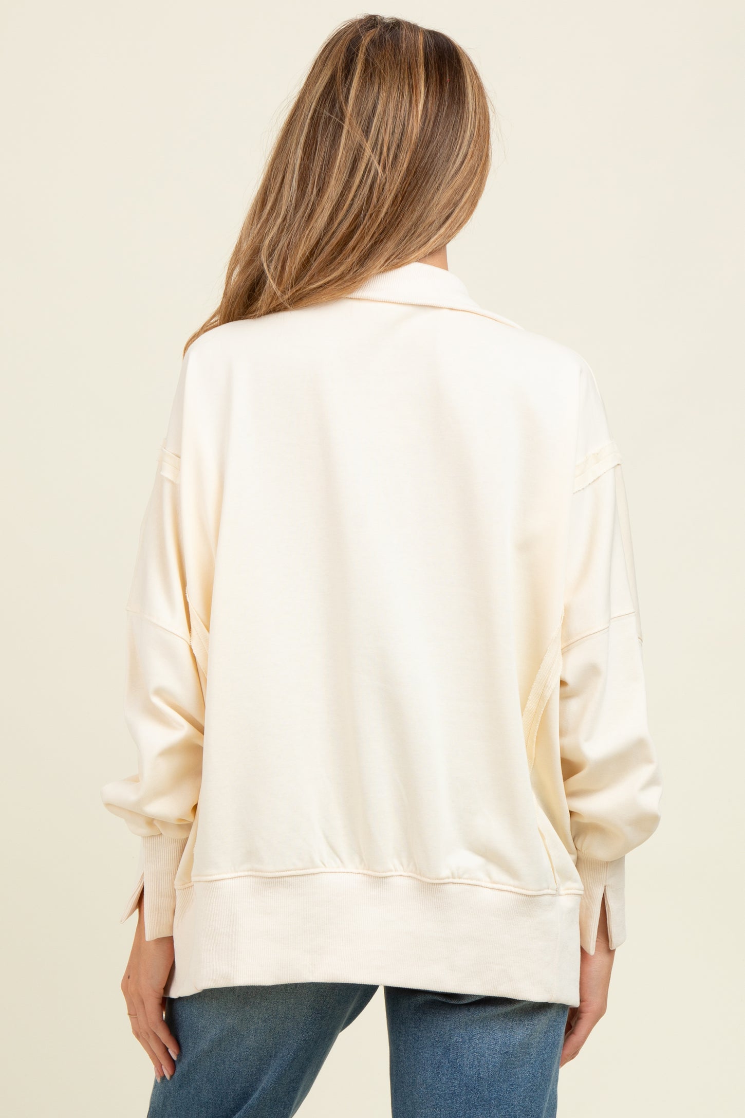 woman wearing a light beige oversized maternity sweatshirt, viewed from the back with relaxed fit and dropped shoulders