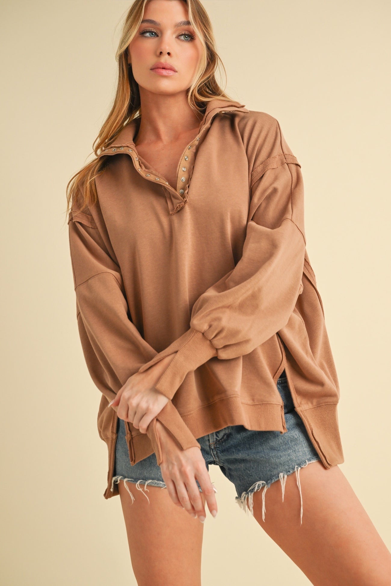 woman wearing a tan oversized pullover with a collar and button detail, paired with distressed denim shorts