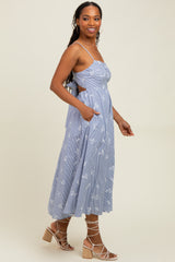 woman wearing a blue and white striped midi dress with floral print and side pockets, standing sideways with a relaxed pose