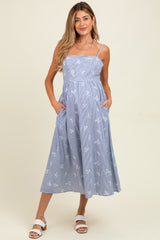 woman wearing a light blue striped maternity dress with white floral embroidery and pockets, standing against a neutral background