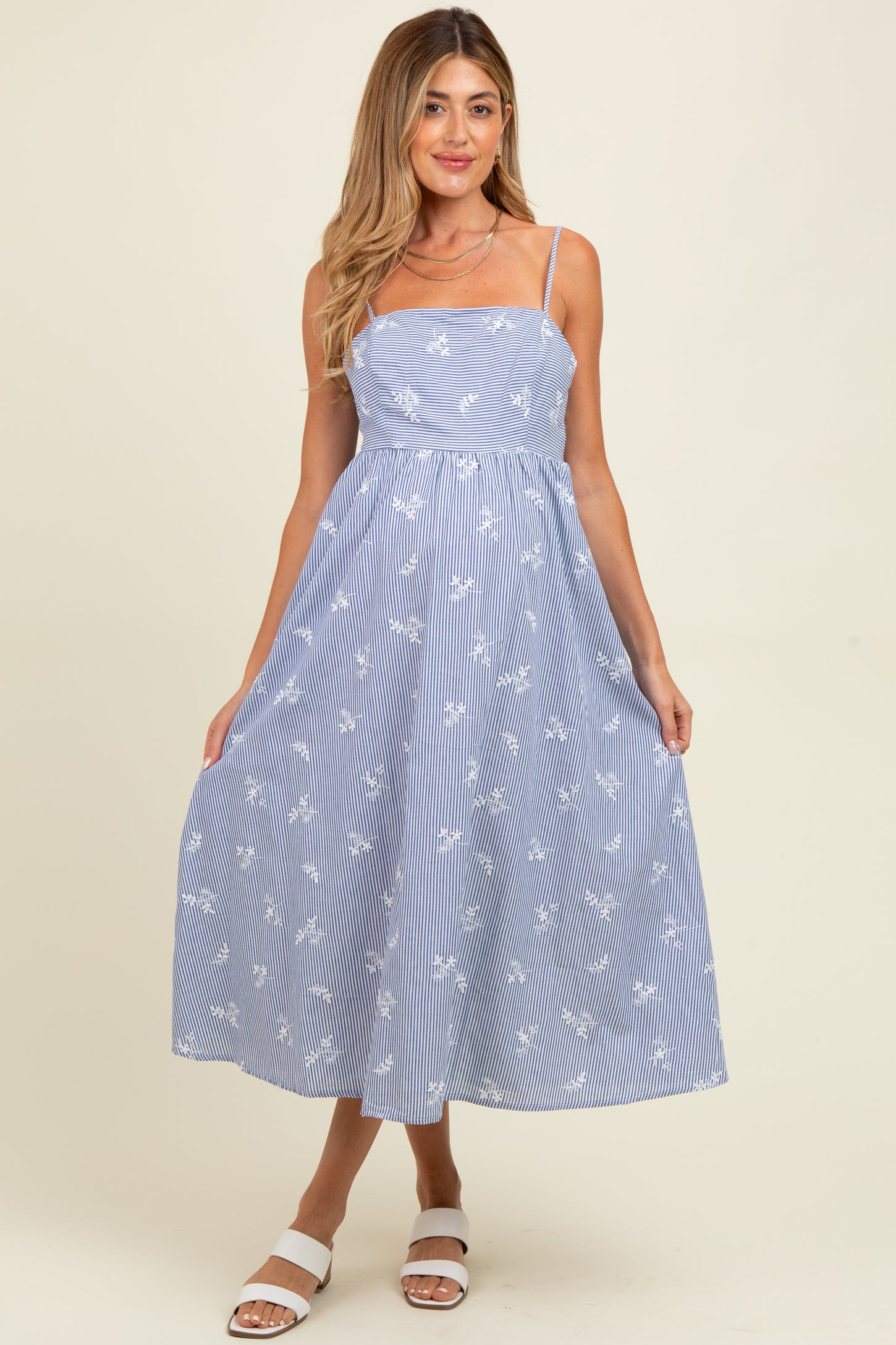 woman wearing a blue and white floral print maternity dress with spaghetti straps and a flowy midi skirt