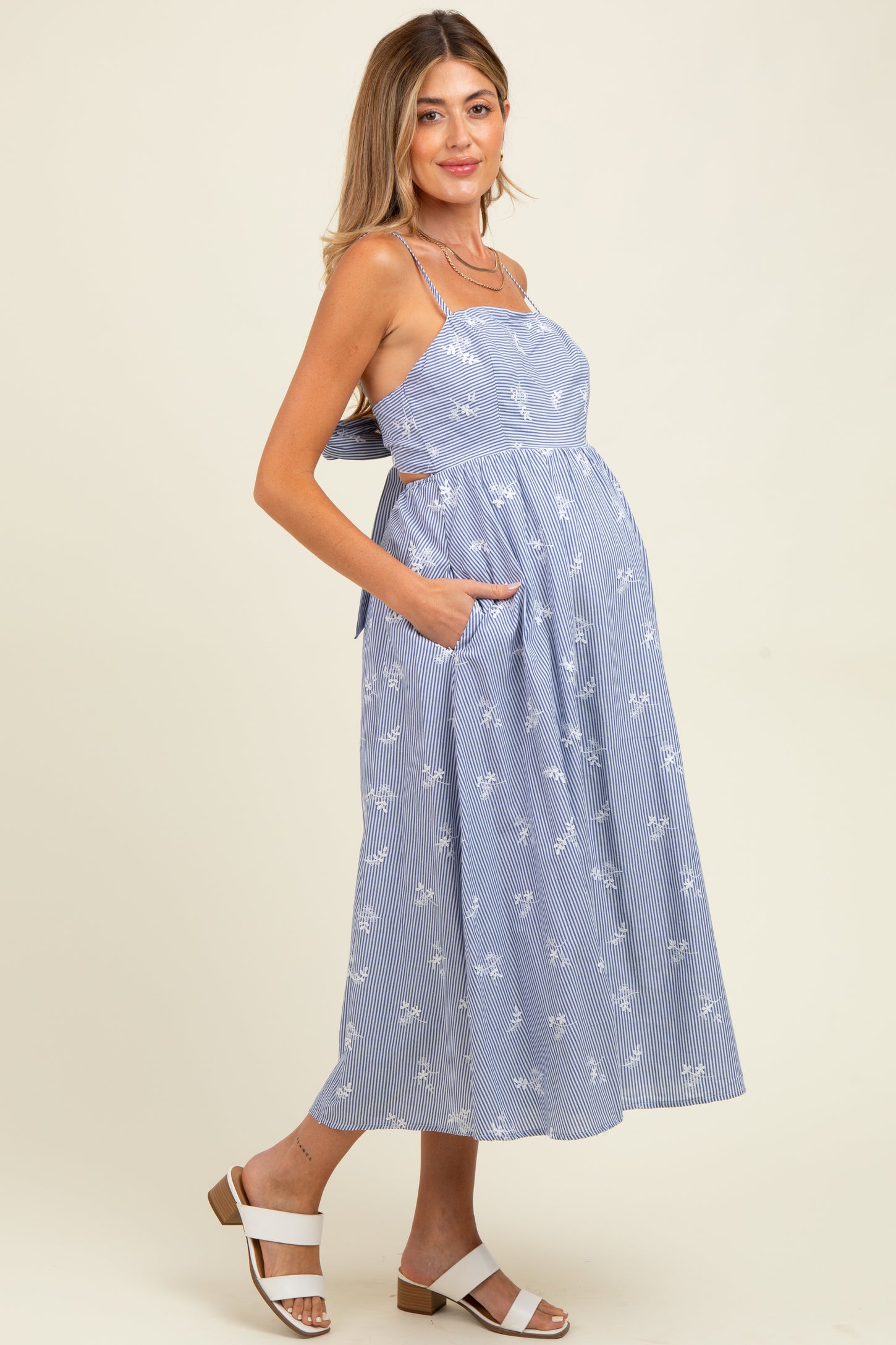 woman wearing a blue striped maternity dress with floral print and pockets, showing off her baby bump