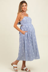 woman wearing a blue striped maternity dress with floral print and pockets, showing off her baby bump