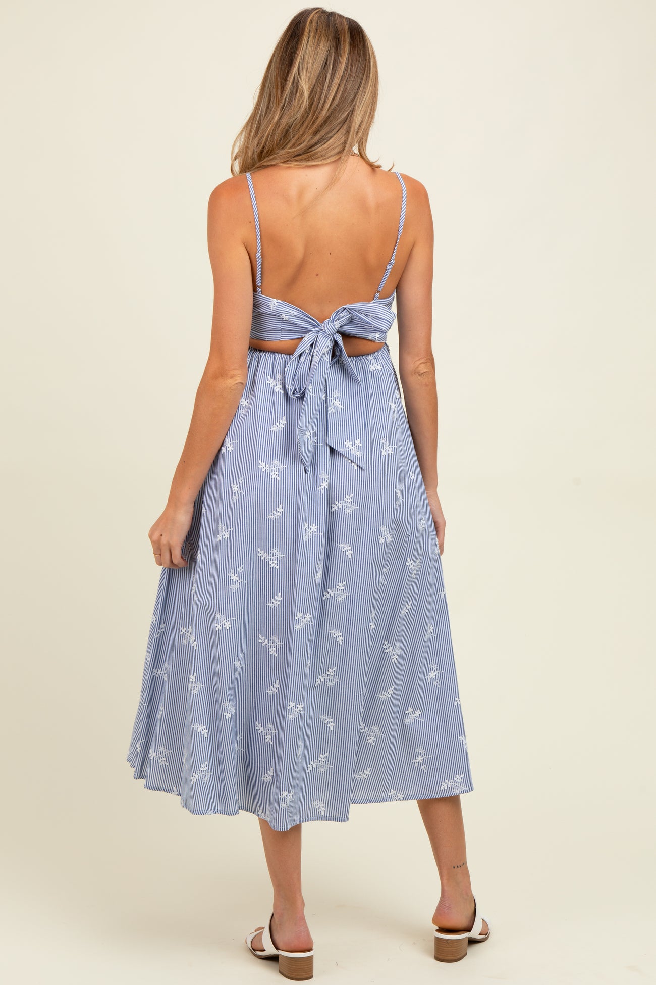 woman wearing a blue and white striped maternity dress with a tie back and floral pattern, showing her baby bump