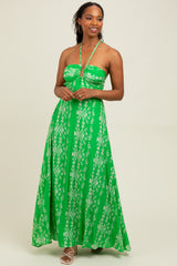 woman wearing a green maxi dress with white floral patterns and a halter neckline, standing against a neutral background