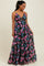 woman wearing a black floral maxi dress with spaghetti straps and a tiered skirt, smiling and standing on a light background