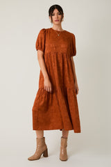 woman wearing a rust colored puff sleeve midi dress with a tiered skirt and light brown ankle boots