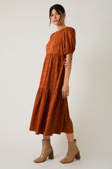 woman wearing a rust colored midi dress with puff sleeves and tiered skirt, paired with ankle boots