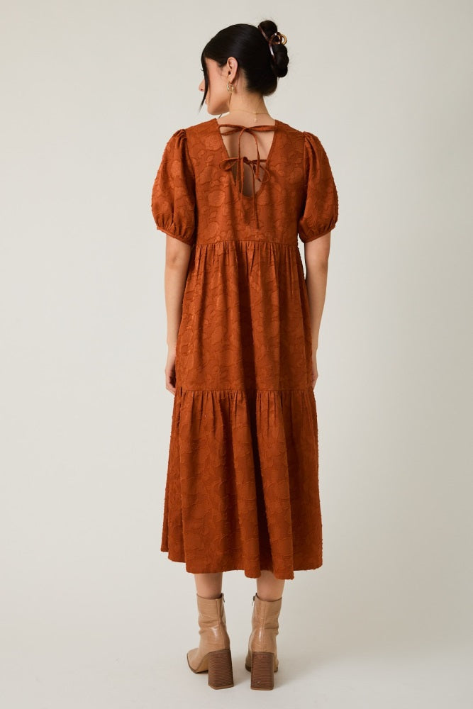 woman wearing a rust-colored tiered maxi dress with puff sleeves and a tie-back detail