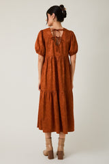 woman wearing a rust-colored tiered maxi dress with puff sleeves and a tie-back detail
