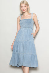 woman wearing a light blue denim sundress with smocked bodice and tiered skirt, featuring adjustable tie straps