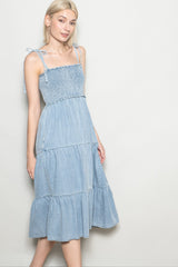 woman wearing a light blue denim tiered midi dress with smocked bodice and spaghetti straps