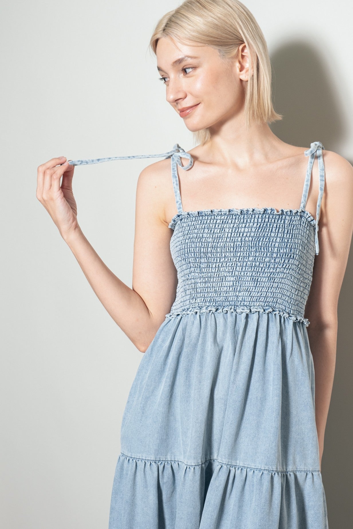 woman wearing a light blue smocked sundress with adjustable tie straps and tiered skirt