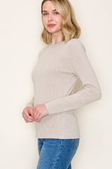 woman wearing a beige ribbed long sleeve top paired with blue jeans
