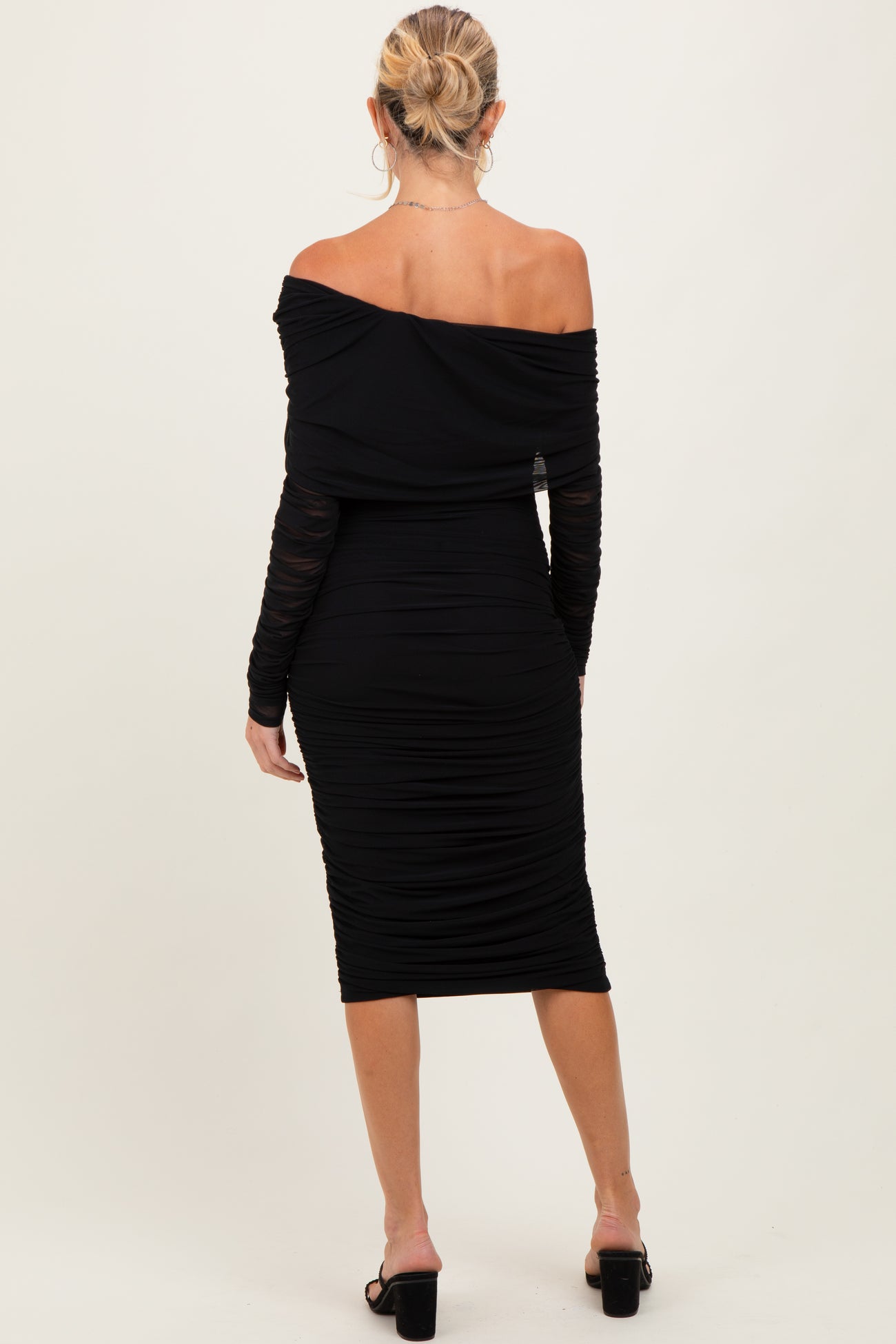 woman wearing a black off-shoulder maternity dress with ruched detailing and long sleeves, showing a baby bump