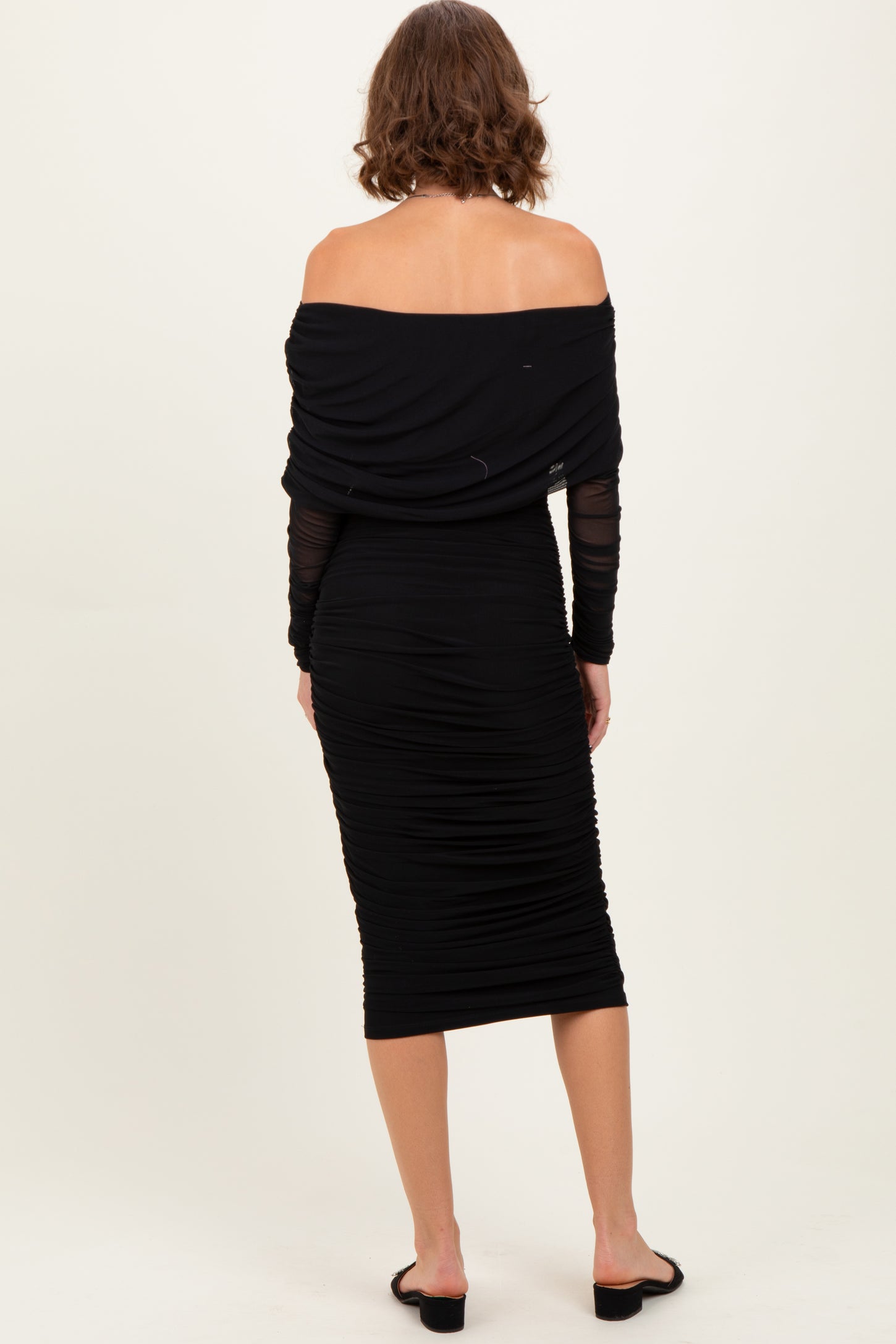 woman wearing a black off-the-shoulder ruched midi dress with long sleeves and a fitted silhouette