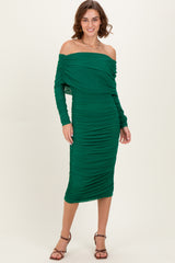 woman wearing a green off-the-shoulder ruched midi dress with long sleeves and a fitted silhouette