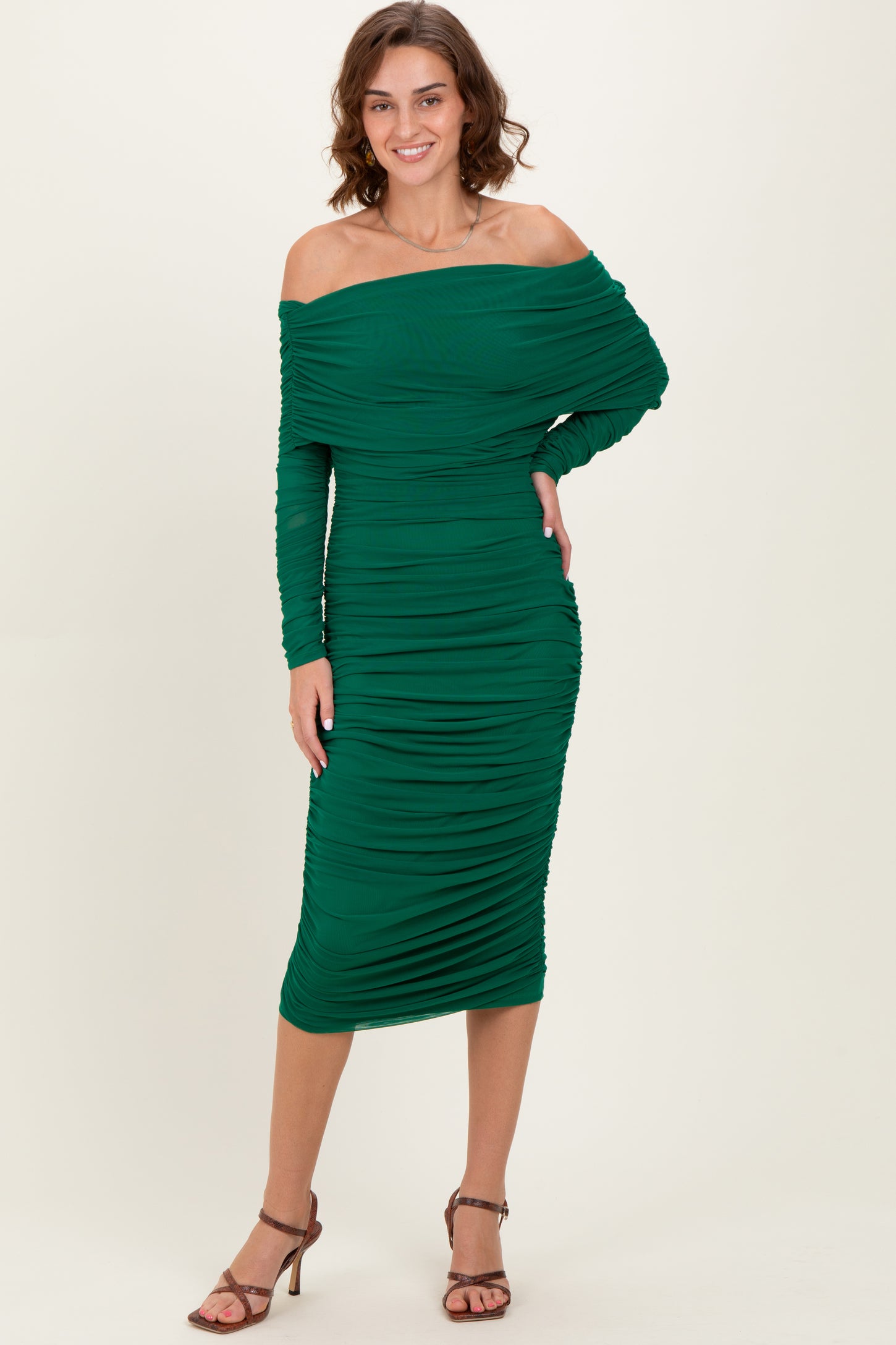 woman wearing a green off-shoulder midi dress with ruched detailing and long sleeves, standing in a relaxed pose