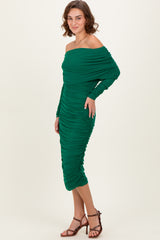 woman wearing a green off-the-shoulder ruched midi dress with long sleeves and a fitted silhouette
