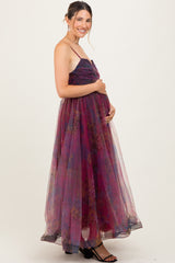 woman wearing a purple floral maternity gown with a flowing skirt, holding her baby bump while smiling
