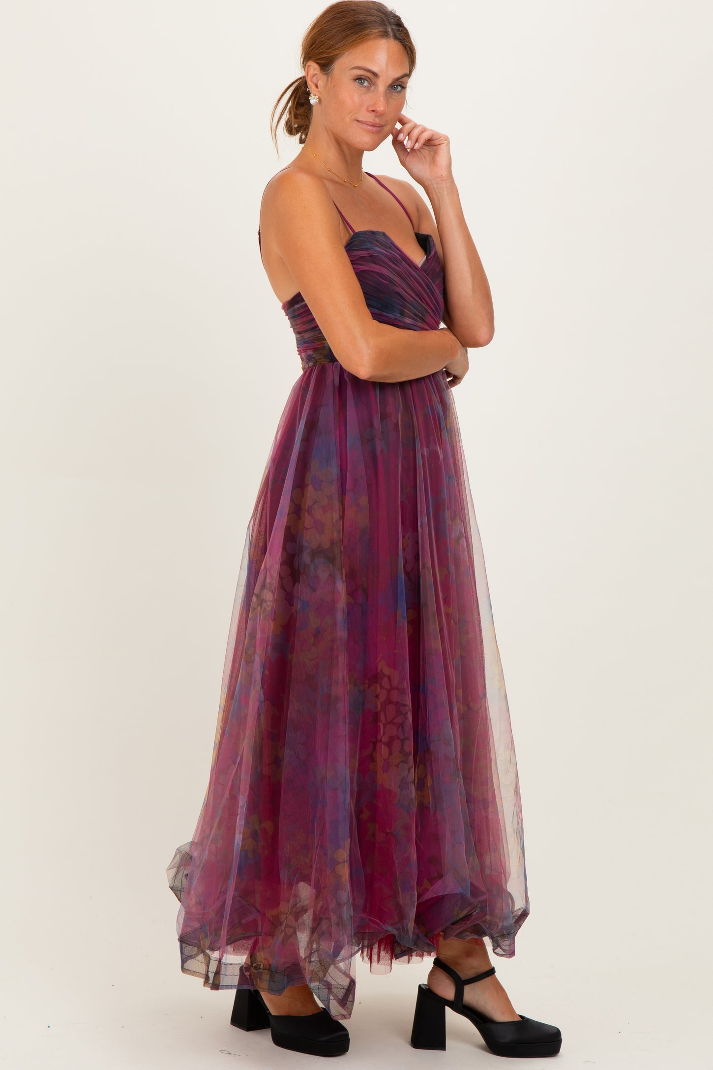 woman wearing a strapless burgundy maxi dress with floral patterns and a flowing tulle skirt, styled with black platform shoes