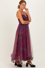woman wearing a strapless burgundy maxi dress with floral patterns and a flowing tulle skirt, styled with black platform shoes