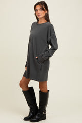 woman wearing a gray long sleeve sweatshirt dress with side pockets and knee-high black leather boots