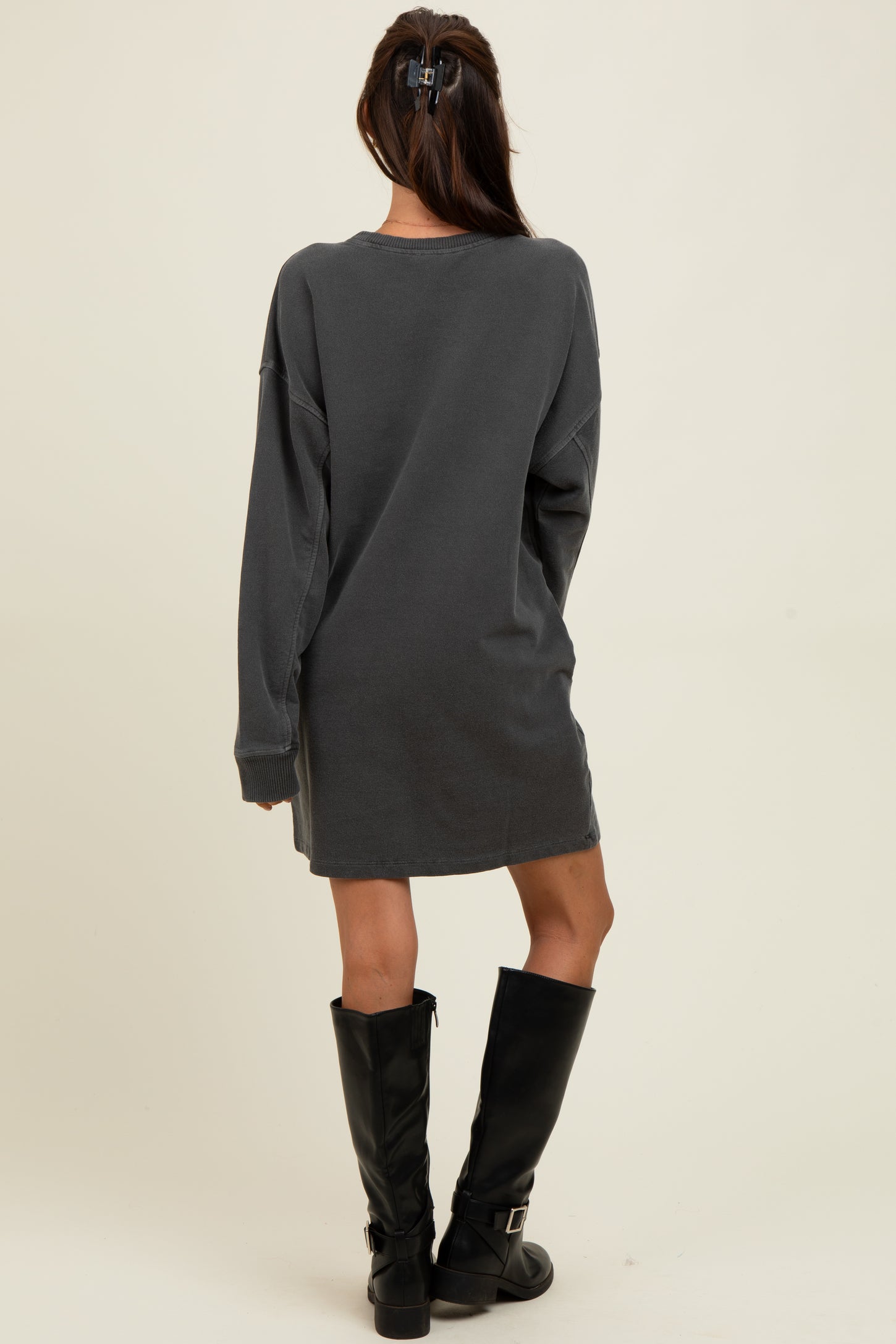 woman wearing a dark grey oversized sweatshirt dress and tall black knee-high boots, facing away from the camera
