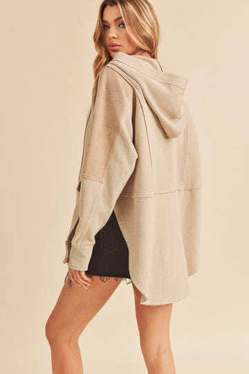 woman wearing a tan oversized hoodie with a hood and frayed hem, styled with a black denim skirt
