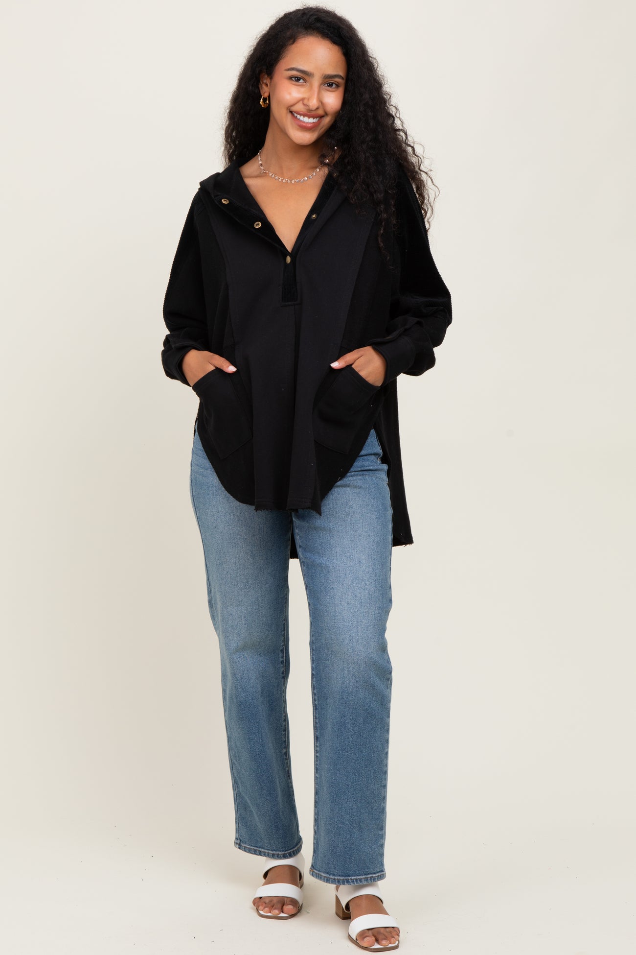 woman wearing a black maternity hoodie with pockets and button detail, paired with light wash jeans and sandals