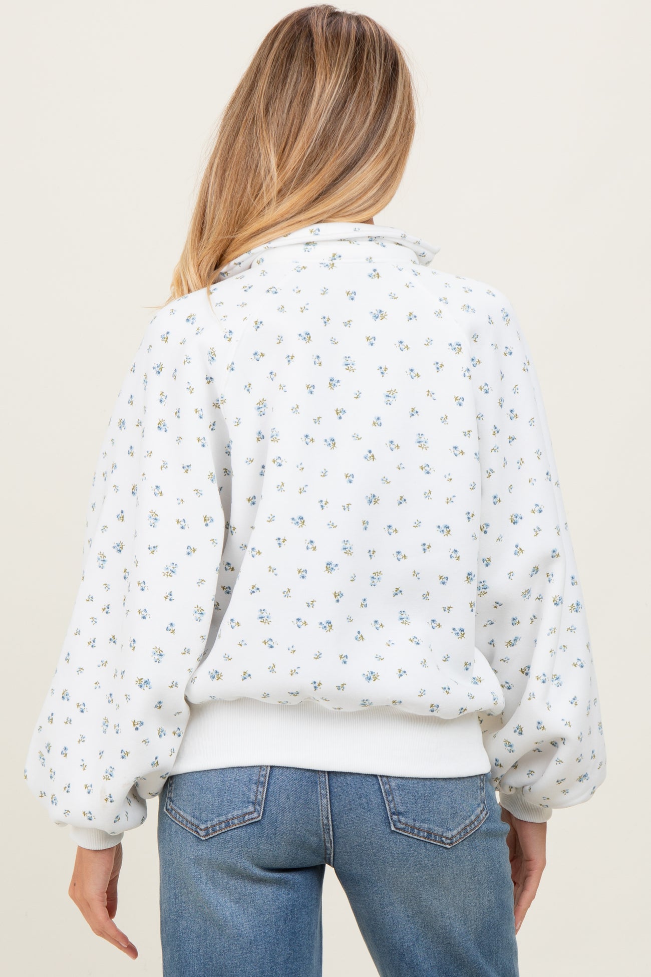woman wearing a white floral print maternity sweatshirt with balloon sleeves and a high collar, shown from the back