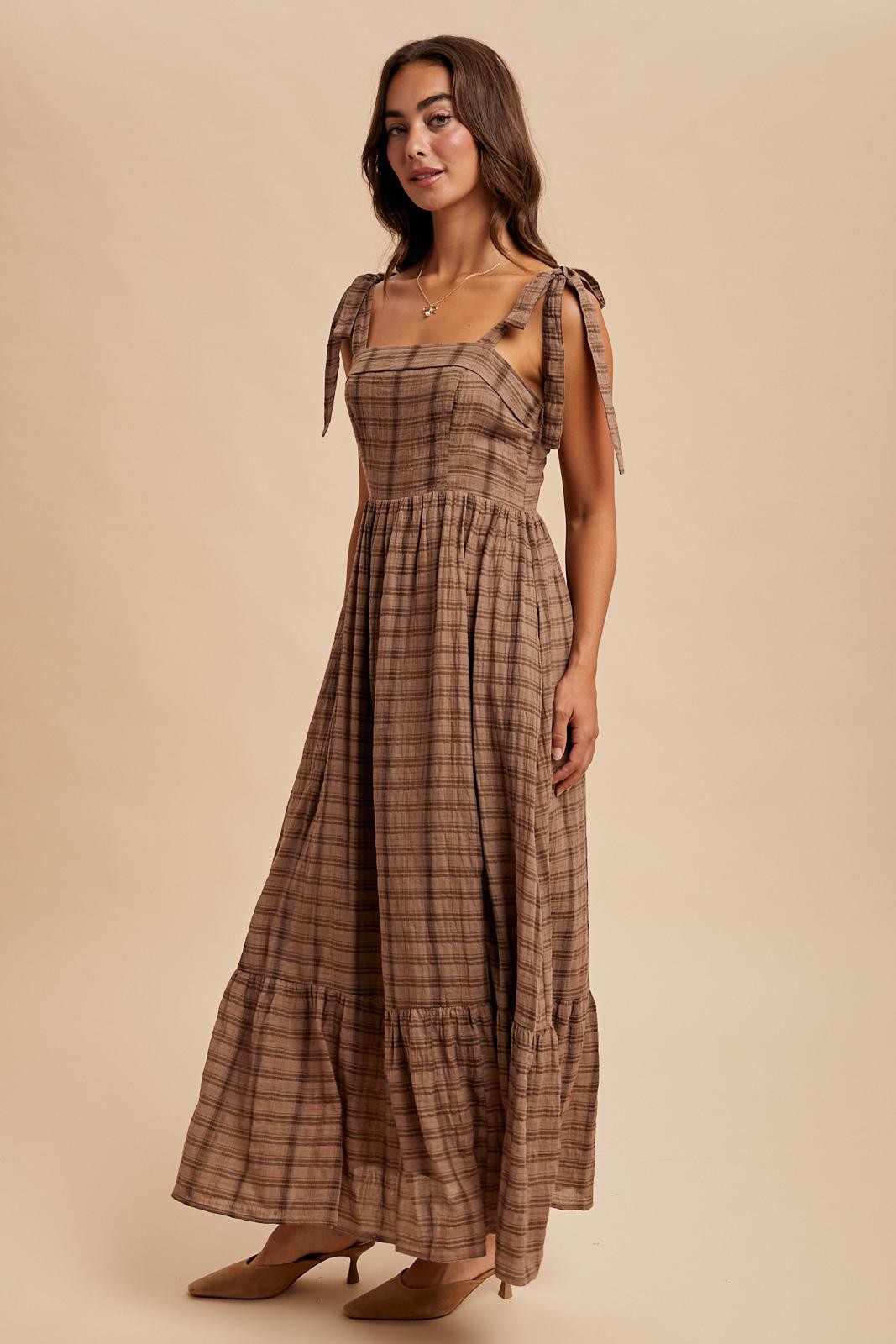 woman wearing a brown plaid maxi dress with tie straps and a ruffled hemline