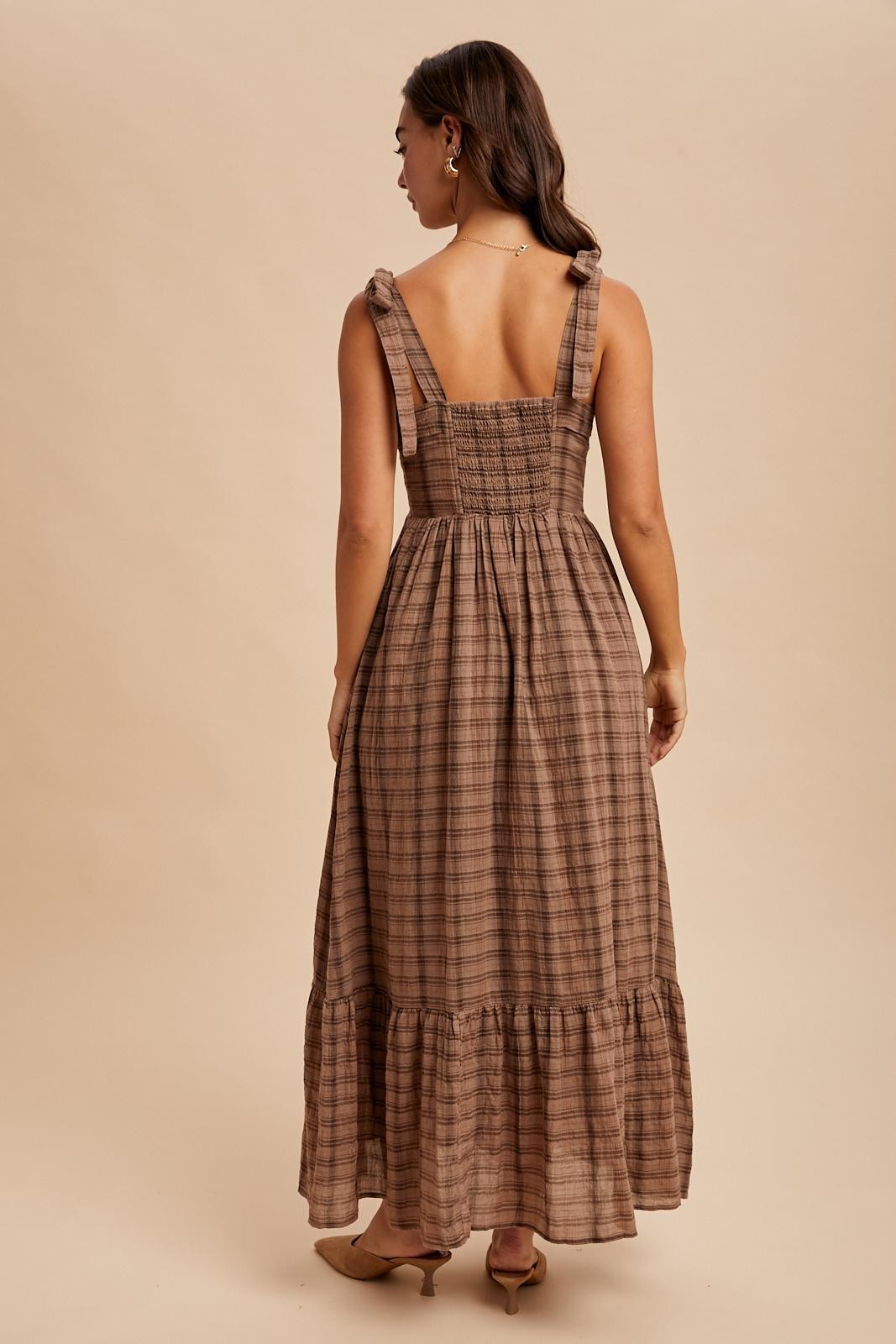 woman wearing a brown plaid maxi dress with ruffled straps and a smocked back, standing against a neutral background