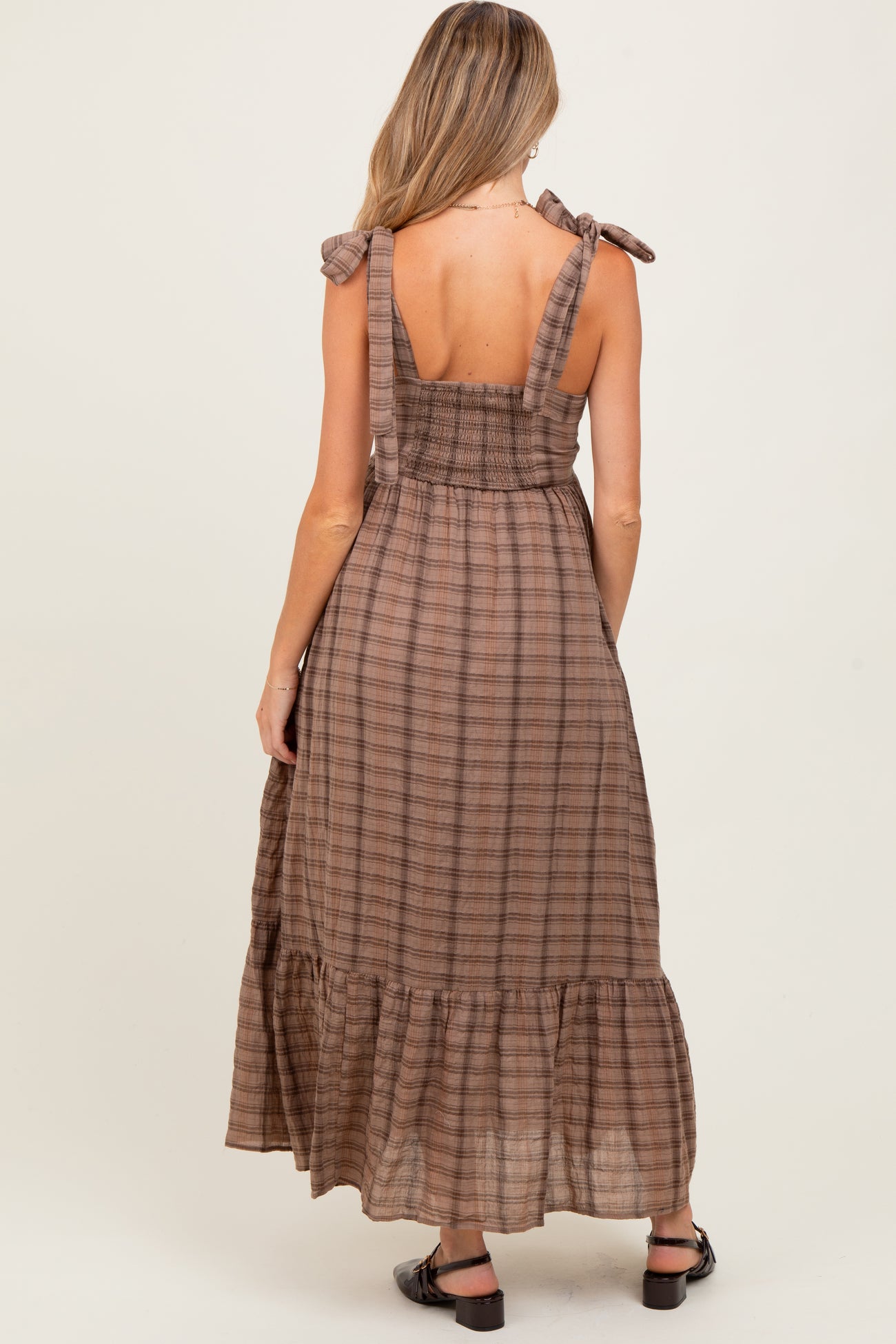 woman wearing a brown plaid maternity maxi dress with bow tie straps and a tiered skirt, showing her back