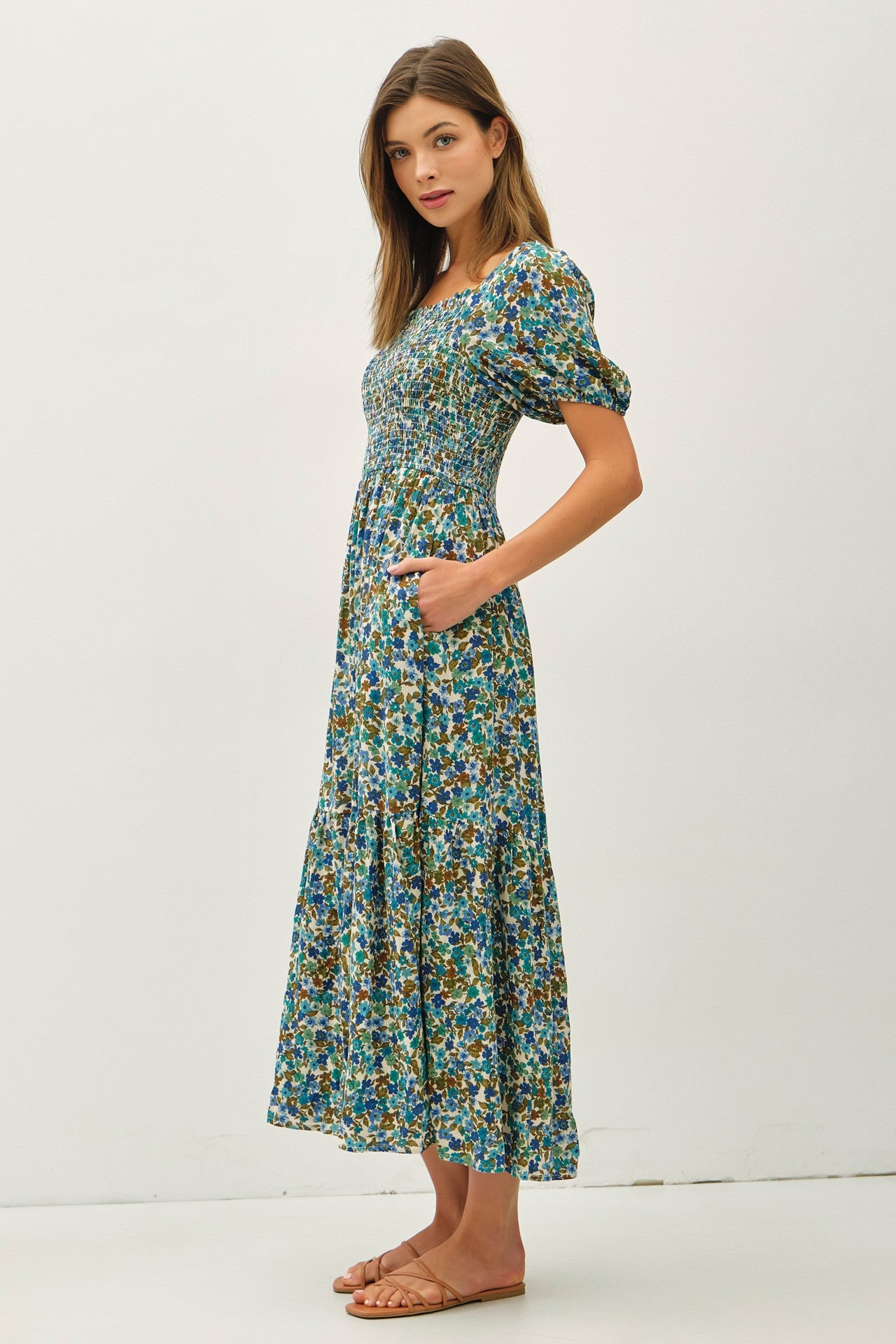 woman wearing a floral maxi dress with short puff sleeves and pockets, standing against a plain background