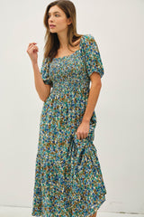 woman wearing a floral midi dress with a smocked bodice and puff sleeves in shades of blue and green