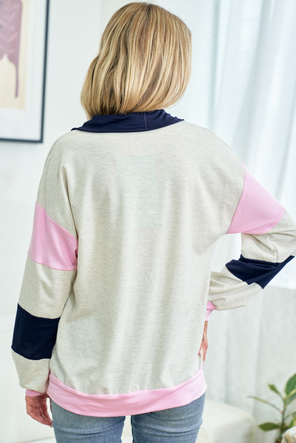 woman wearing a light gray sweatshirt with pink and navy color-block stripes, viewed from the back