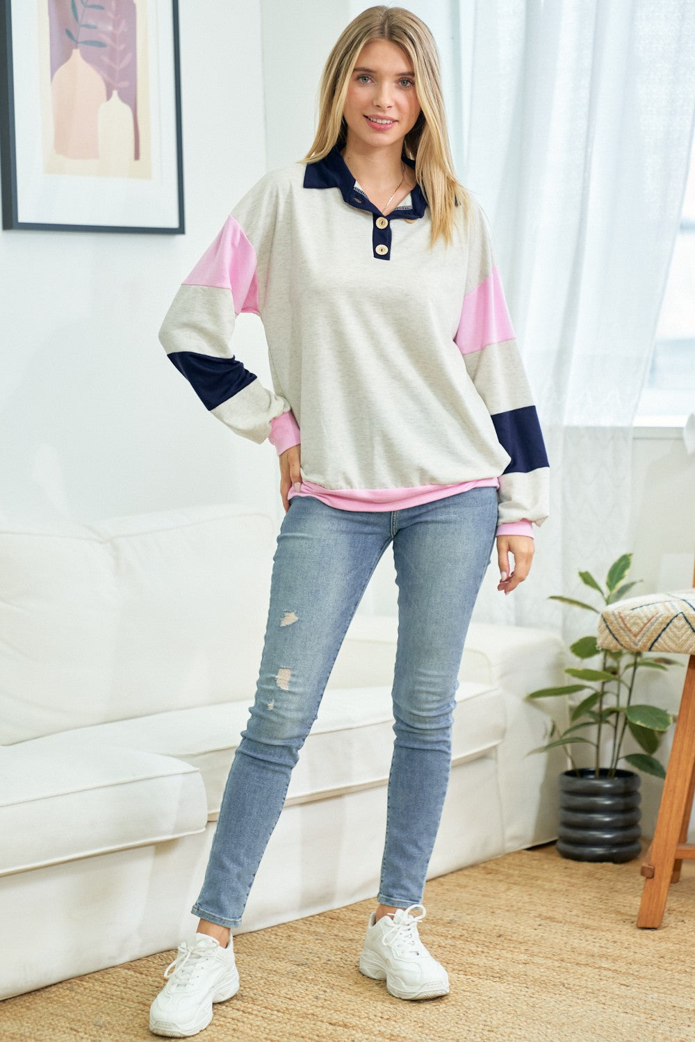 woman wearing a light gray colorblock long sleeve pullover with pink and navy accents, paired with distressed skinny jeans