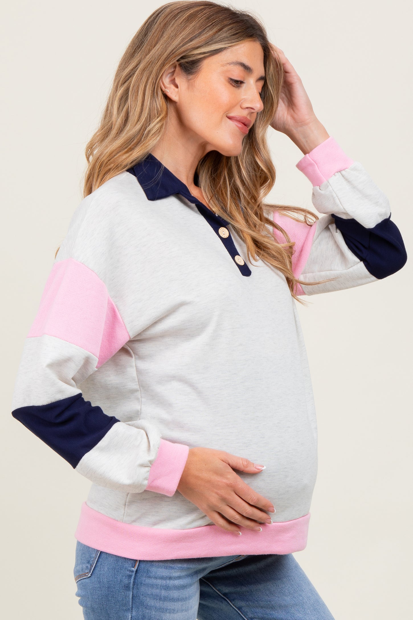 woman wearing a light gray maternity sweatshirt with pink and navy sleeves, showing her baby bump while smiling