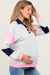 woman wearing a light gray maternity sweatshirt with pink and navy sleeves, showing her baby bump while smiling