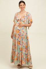 woman wearing a floral green maternity maxi dress with a deep v-neck and tie detail, holding her baby bump