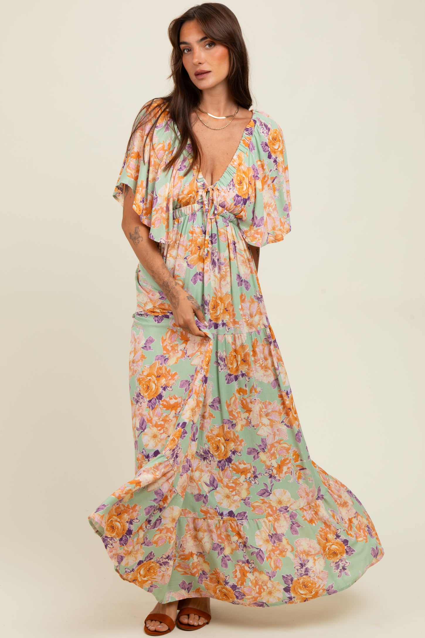 woman wearing a floral maxi dress with flutter sleeves in pastel green, yellow, and orange tones, twirling gracefully