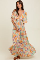 woman wearing a floral maxi dress with flutter sleeves in pastel green, yellow, and orange tones, twirling gracefully